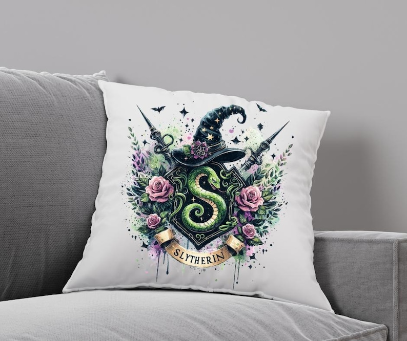 May include: A white pillow with a watercolor illustration of the Slytherin house crest from the Harry Potter series. The crest features a green snake, a wizard's hat, and the words "Slytherin" in gold lettering.