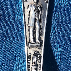 May include: Silver souvenir spoon with a design featuring the Chicago Public Library, Lincoln Statue, and Douglas Monument. The spoon has the letters "CH" at the bottom.