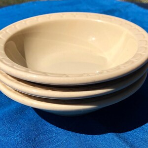 May include: Three ivory-colored ceramic bowls with a decorative rim. The bowls are stacked on top of each other.