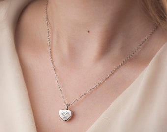 May include: A silver chain necklace with a heart-shaped pendant featuring a cluster of small, clear gemstones.
