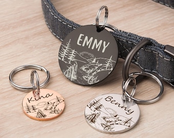 May include: Three personalized dog tags with a mountain scene engraved on each. The tags are silver, black, and rose gold. The names "Emmy", "Kina", and "Benny" are engraved on the tags.