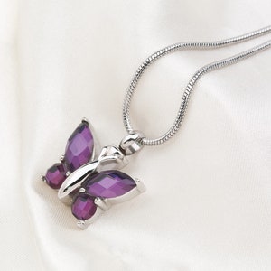 May include: A silver chain necklace with a purple butterfly pendant. The butterfly is made of faceted glass and has a silver setting.