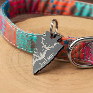 May include: A black metal dog tag with a deer silhouette and the name "Jackson" engraved on it. The tag is attached to a colorful patterned dog collar.