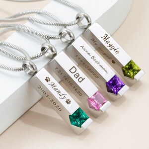 May include: Four silver necklaces with engraved rectangular pendants. Each pendant has a different colored gemstone at the bottom. The pendants are engraved with names, dates, and a paw print. The text on the pendants reads: "Maggie My angel", "Anna Bachman 1999&hearts;2020", "Dad 7.21.74-10.14.20", and "Mandy 2001-2020".