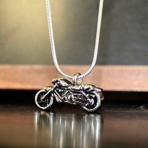 Puede incluir: Un collar de cadena de plata con un colgante de motocicleta de plata. La motocicleta est&aacute; detallada y tiene un dise&ntilde;o realista.