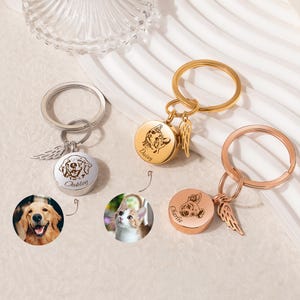 May include: Three pet memorial keychains in silver, gold, and rose gold. Each keychain features a round pendant with a pet portrait and name, accompanied by a small wing charm. The pendants showcase a dog and a cat.