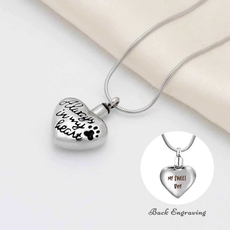May include: Silver heart-shaped cremation necklace with a chain. The front of the pendant has the inscription "Always in my heart" and a paw print. The back of the pendant has the inscription "My Sweet Boy".