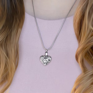 May include: A silver heart-shaped cremation necklace with the inscription "Always in my heart" and a paw print. The necklace is on a silver chain.