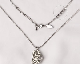 Könnte beinhalten: Eine silberne Halskette mit einem herzförmigen Anhänger, der ein Fingerabdruckdesign aufweist. Die Halskette hat eine Kette mit einem Karabinerverschluss und eine Verlängerungskette.