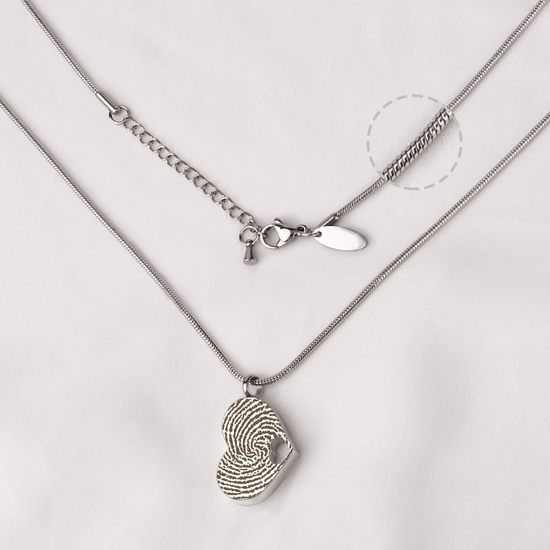 Puede incluir: Un collar de plata con un colgante en forma de coraz&oacute;n que presenta un dise&ntilde;o de huella digital. El collar tiene una cadena con un cierre de langosta y una cadena extensora.