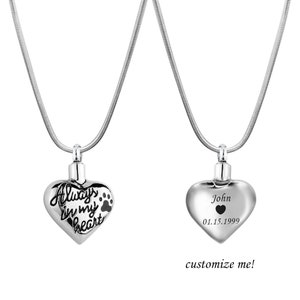 May include: Two silver heart-shaped cremation necklaces. One necklace has the inscription "Always in my heart" with a paw print. The other necklace has the inscription "John 01.15.1999".