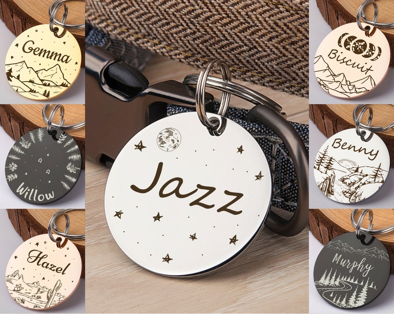 Op de afbeelding: Een assortiment gepersonaliseerde hondenpenningen met verschillende ontwerpen. De penningen zijn gegraveerd met namen zoals "Gemma", "Willow", "Hazel", "Jazz", "Biscuit", "Benny" en "Murphy". Elke penning heeft een uniek ontwerp met een berg-, bos- of hemelthema.