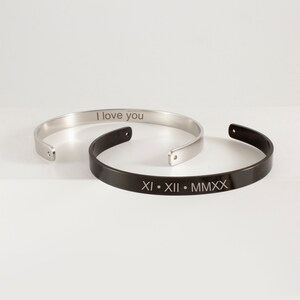 Op de afbeelding: Twee gegraveerde armbanden van roestvrij staal. Een armband is zilver en gegraveerd met "I love you". De andere armband is zwart en gegraveerd met "XI. XII. MMXX".
