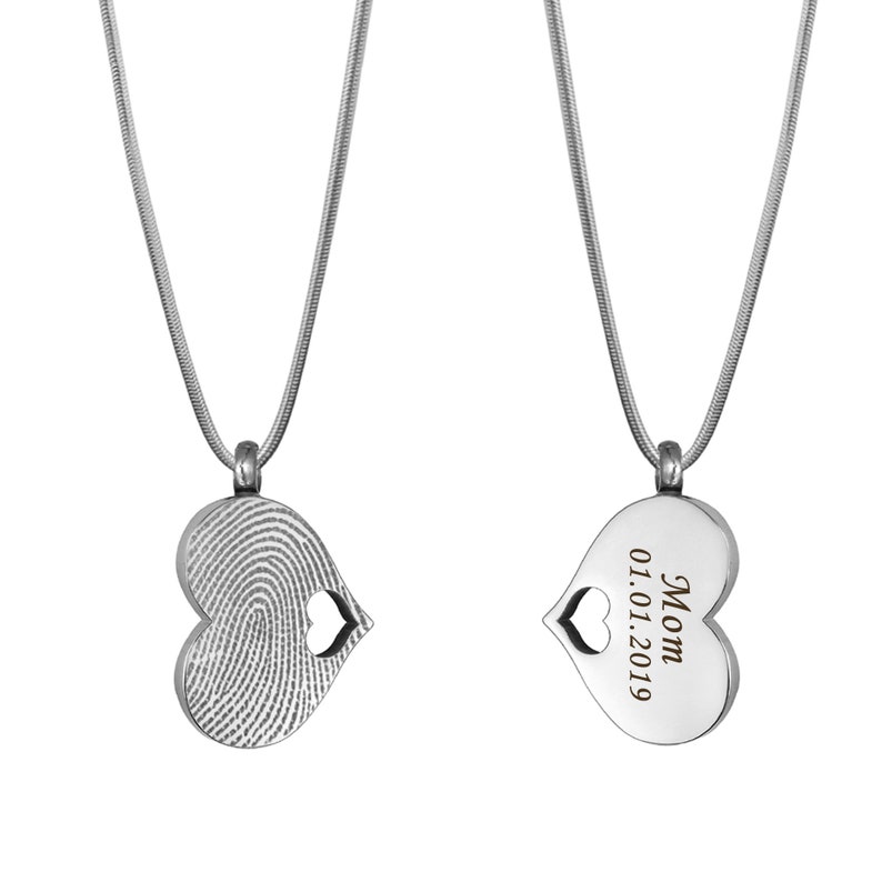 Puede incluir: Dos collares de cremaci&oacute;n de coraz&oacute;n plateado. Un collar presenta un dise&ntilde;o de huella digital, mientras que el otro tiene la inscripci&oacute;n "Mam&aacute; 01.01.2019".