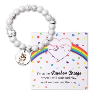 May include: White marble bead bracelet with a silver paw print charm, a heart charm, and a round silver charm with a dog silhouette and the name "Hazel" engraved on it. The bracelet comes with a card that reads "I'm at the Rainbow Bridge where I will wait and play, until we meet another day."