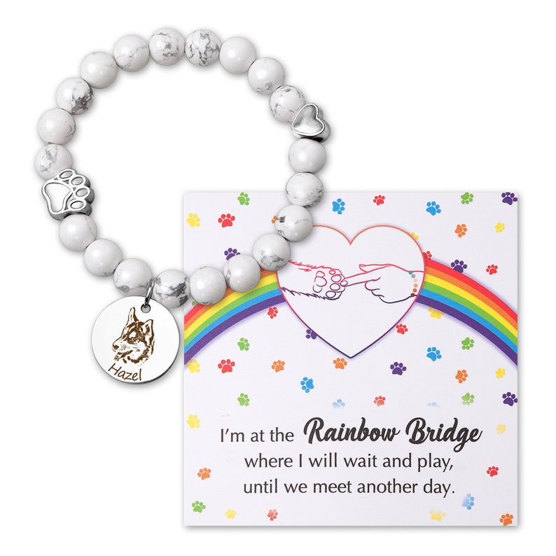 May include: White marble bead bracelet with a silver paw print charm, a heart charm, and a round silver charm with a dog silhouette and the name "Hazel" engraved on it. The bracelet comes with a card that reads "I'm at the Rainbow Bridge where I will wait and play, until we meet another day."