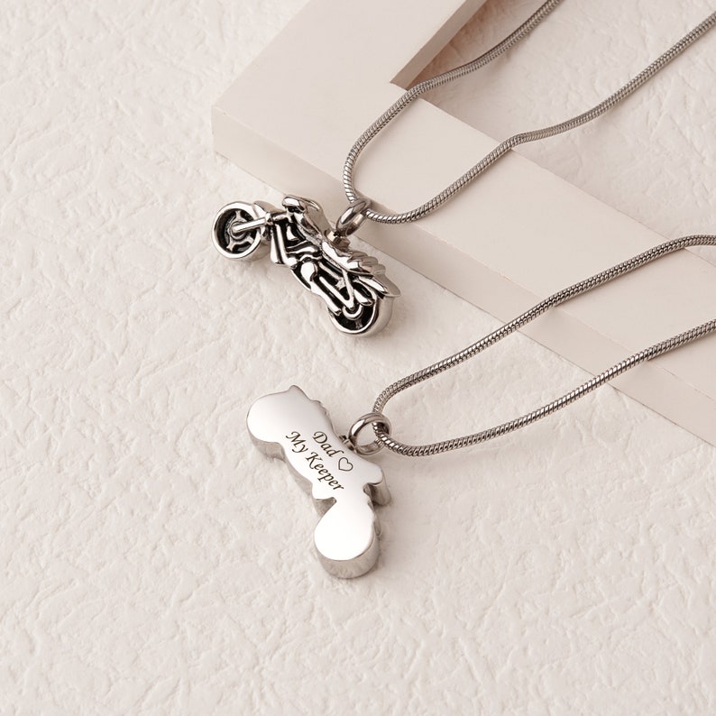 Puede incluir: Dos collares de plata con colgantes de motocicleta. Un colgante es un dise&ntilde;o de motocicleta detallado, mientras que el otro tiene las palabras "Dad My Keeper" grabadas.