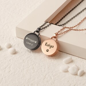 K&ouml;nnte beinhalten: Zwei personalisierte Tier-Gedenk-Halsketten. Eine ist schwarz mit der Aufschrift "Maggie Love U" und einem Pfotenabdruck. Die andere ist ros&eacute;goldfarben mit der Aufschrift "Kaiya" und einem Pfotenabdruck.
