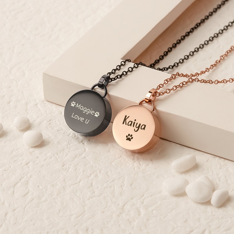 K&ouml;nnte beinhalten: Zwei personalisierte Tier-Gedenk-Halsketten. Eine ist schwarz mit der Aufschrift "Maggie Love U" und einem Pfotenabdruck. Die andere ist ros&eacute;goldfarben mit der Aufschrift "Kaiya" und einem Pfotenabdruck.