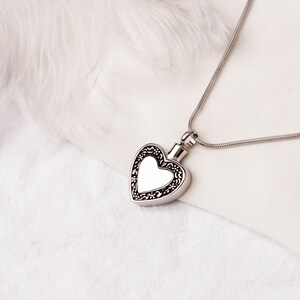 May include: A silver heart-shaped pendant necklace with a detailed filigree design. The pendant has a smooth, reflective surface.