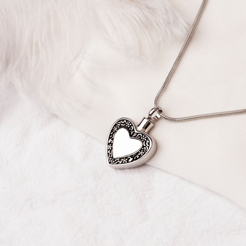 May include: A silver heart-shaped pendant necklace with a detailed filigree design. The pendant has a smooth, reflective surface.