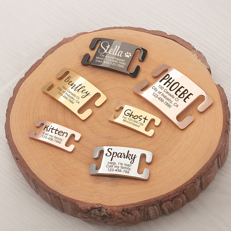 May include: Six different personalized dog tags with engraved text and contact information. The tags are made of metal and have a clip-on design. The tags are displayed on a wooden surface.