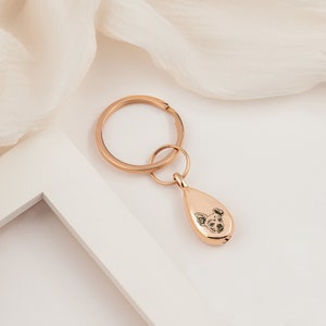 Peut inclure: Porte-cl&eacute;s en m&eacute;tal ton or rose avec un charme en forme de larme orn&eacute; d'une image grav&eacute;e en noir et blanc d'un visage de chien.