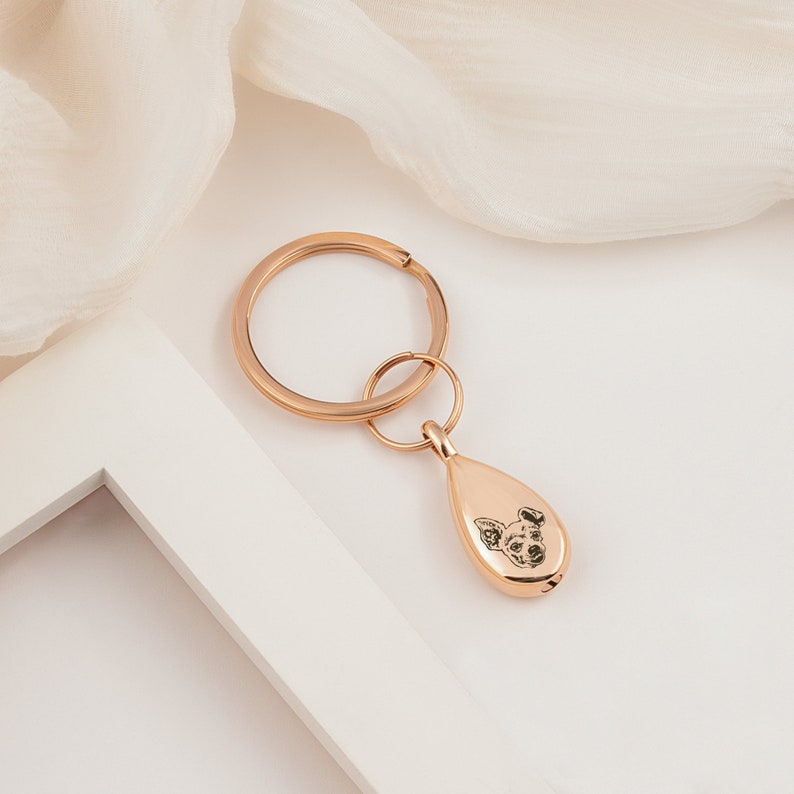 Peut inclure: Porte-cl&eacute;s en m&eacute;tal ton or rose avec un charme en forme de larme orn&eacute; d'une image grav&eacute;e en noir et blanc d'un visage de chien.