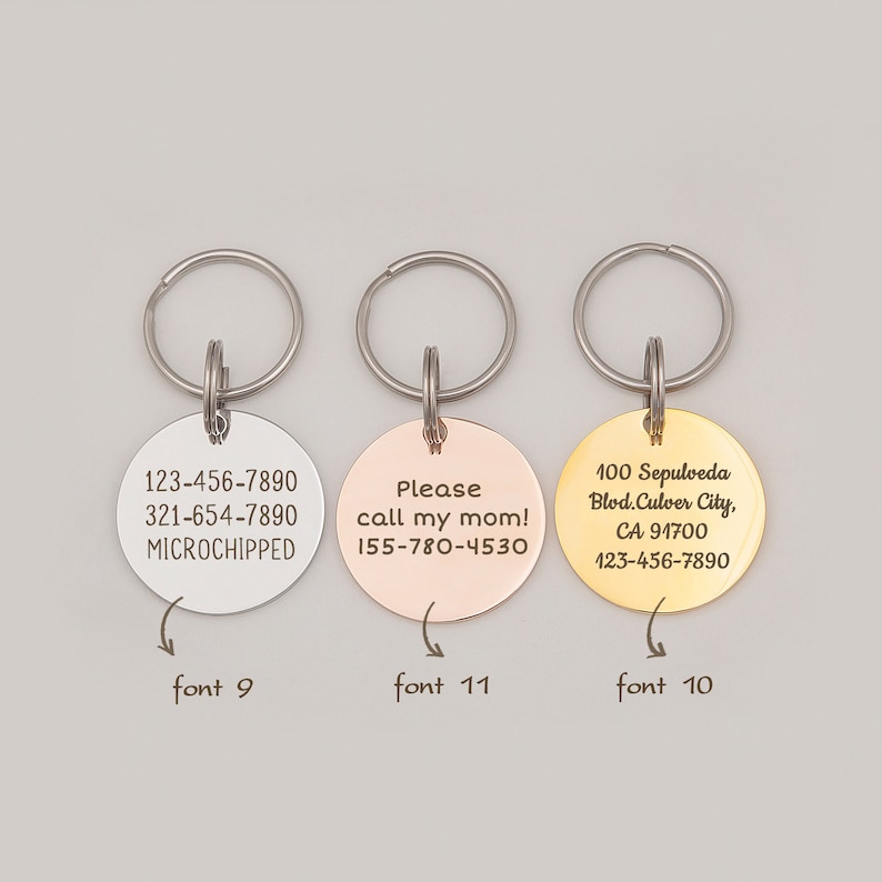 May include: Three round metal dog tags with key rings. The first tag is silver and says "123-456-7890 321-654-7890 MICROCHIPPED". The second tag is rose gold and says "Please call my mom! 155-780-4530". The third tag is gold and says "100 Sepulveda Blod.Culver City, CA 91700 123-456-7890".