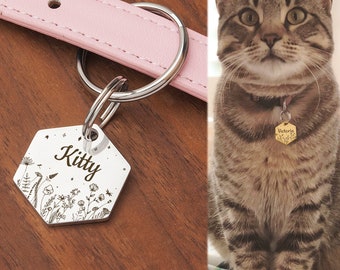 May include: A silver hexagonal pet tag engraved with the name "Kitty" and floral designs, attached to a pink leather collar. The tag is connected to a silver ring. A tabby cat is wearing a similar tag that says "Victoria".