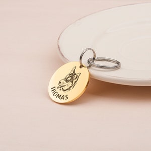 May include: Gold-colored dog tag with a black and white image of a dog's head and the name "THOMAS" engraved on the front.