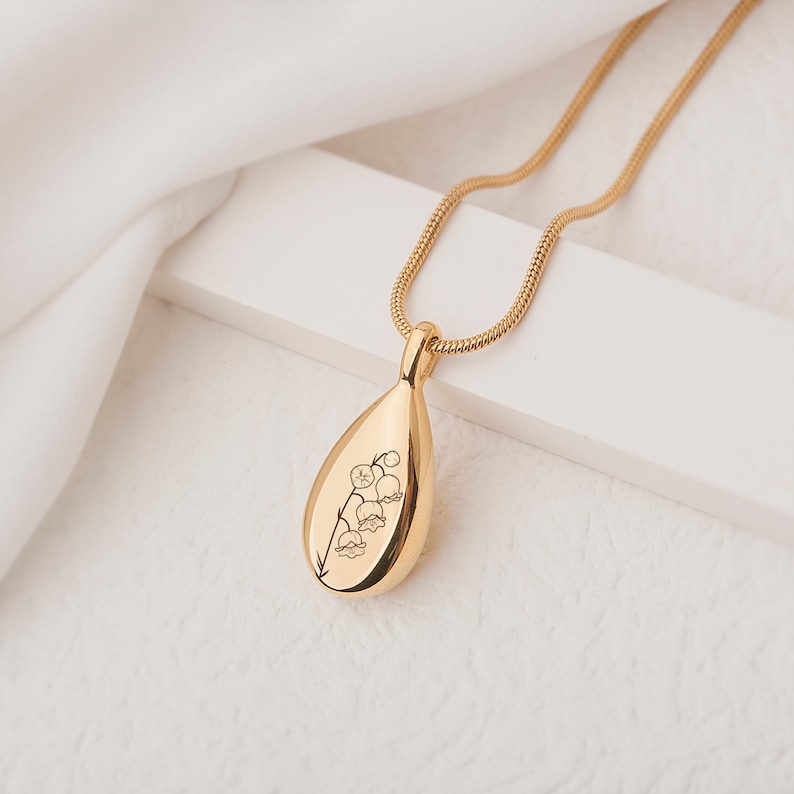 May include: A gold teardrop-shaped pendant necklace with a delicate engraved design of lily of the valley flowers.