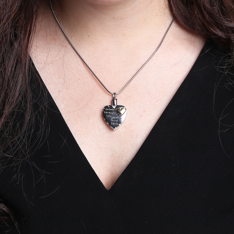 May include: A silver heart-shaped pendant necklace with a gold heart charm. The pendant has an inscription that reads "In loving memory of a life well lived".