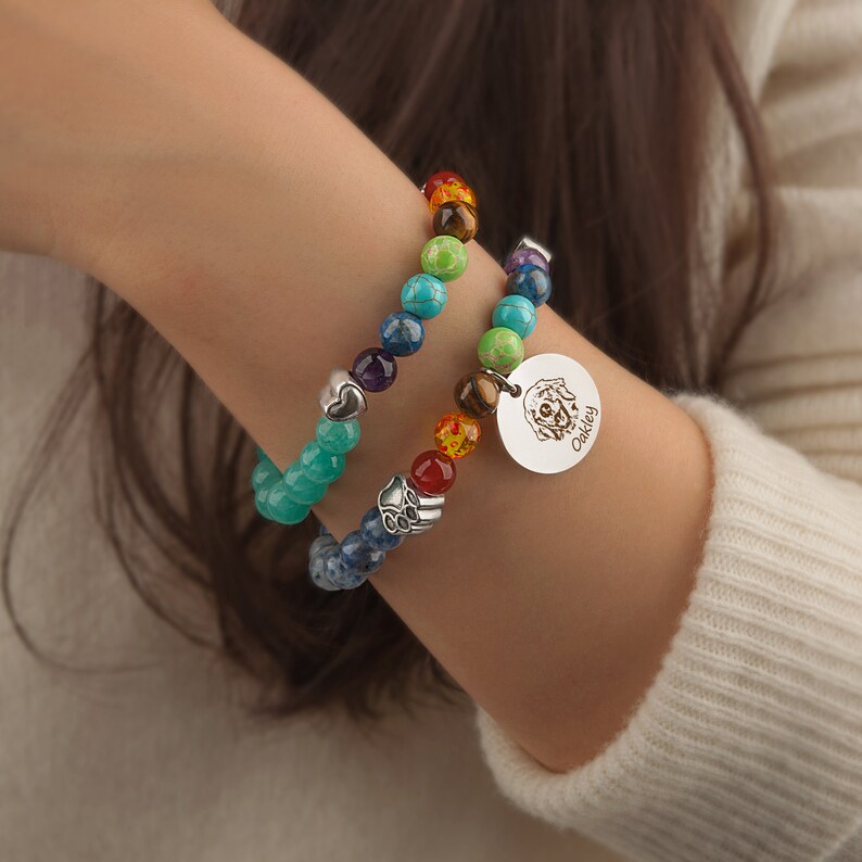 May include: Two beaded bracelets with a charm featuring a dog's face and the name "Oakley" engraved on it. The bracelets are made with colorful gemstones and silver beads.