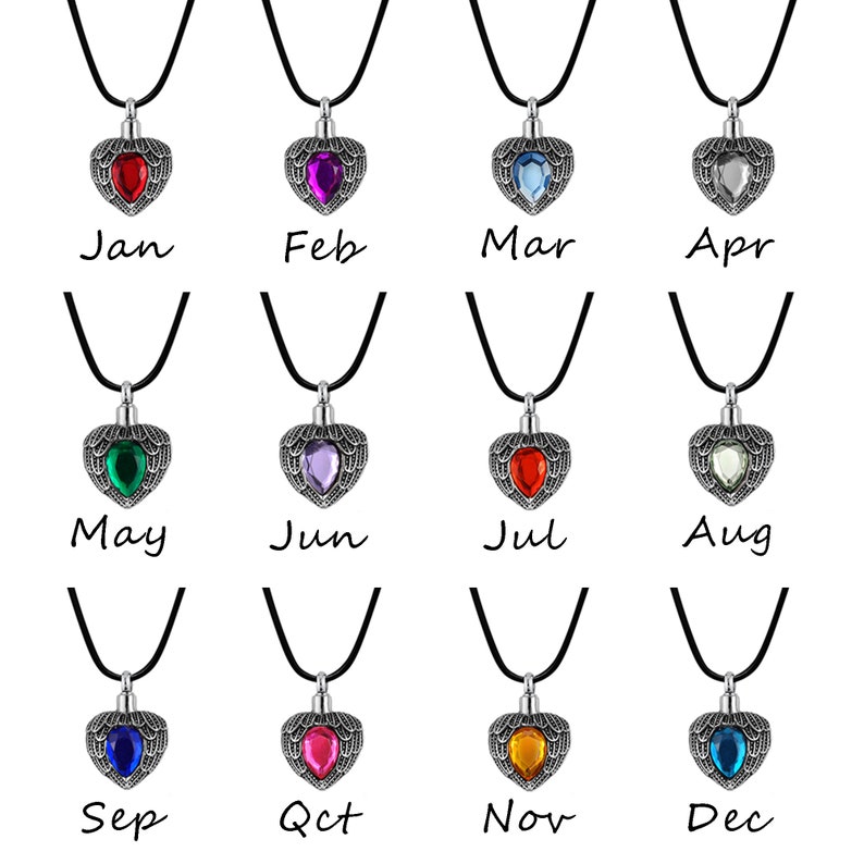 May include: Twelve silver heart-shaped cremation pendants with different colored gemstones. Each pendant is on a black cord and labeled with a month of the year, from January to December.