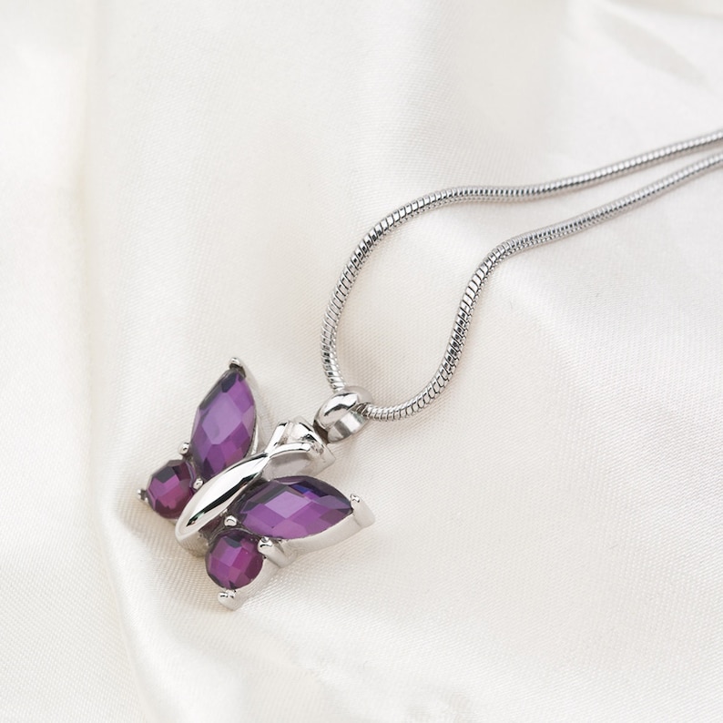 May include: A silver chain necklace with a purple butterfly pendant. The butterfly is made of faceted glass and has a silver setting.