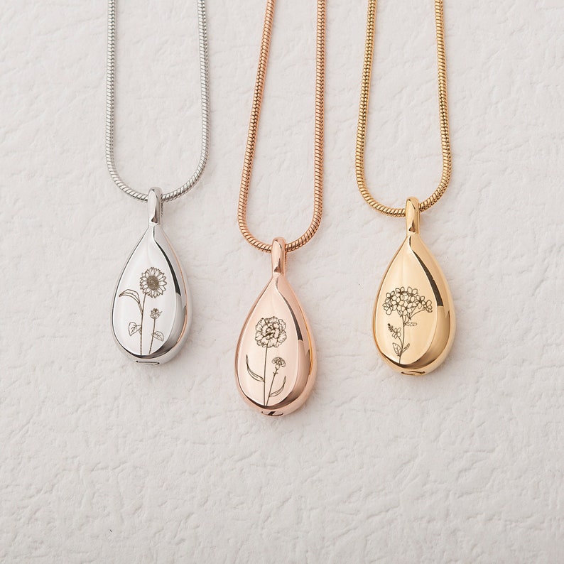 May include: Three silver, rose gold, and gold teardrop necklaces with engraved floral designs. Each necklace features a delicate chain and a pendant with a different floral motif.