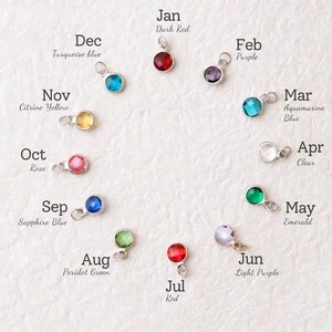 May include: A collection of twelve gemstone charms, each representing a month of the year. The charms are in various colors, including red, purple, blue, green, and yellow, with the month's name and color description next to each charm.