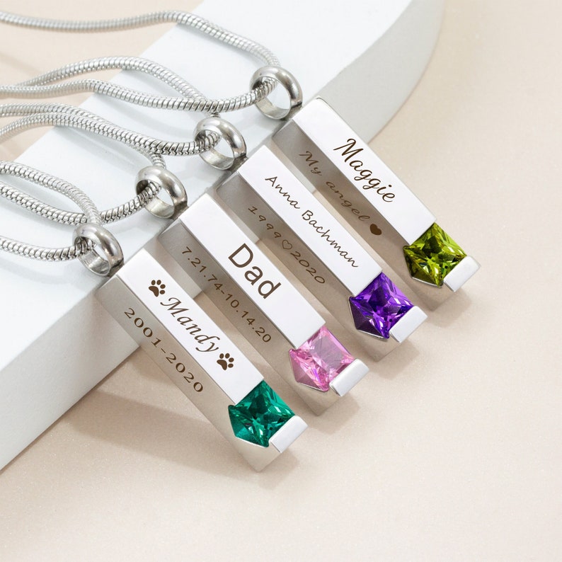 May include: Four silver necklaces with engraved rectangular pendants. Each pendant has a different colored gemstone at the bottom. The pendants are engraved with names, dates, and a paw print. The text on the pendants reads: "Maggie My angel", "Anna Bachman 1999&hearts;2020", "Dad 7.21.74-10.14.20", and "Mandy 2001-2020".