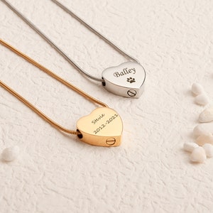 Pu&ograve; includere: Due collane crematorie a forma di cuore, una in oro e una in argento, con nomi e date incisi. La collana d'oro dice "Stevie 2012-2021" e la collana d'argento dice "Bailey" con un'impronta di zampa.