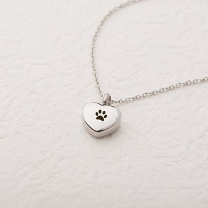 May include: A silver heart-shaped pendant necklace with a paw print cutout. The necklace is on a white background.
