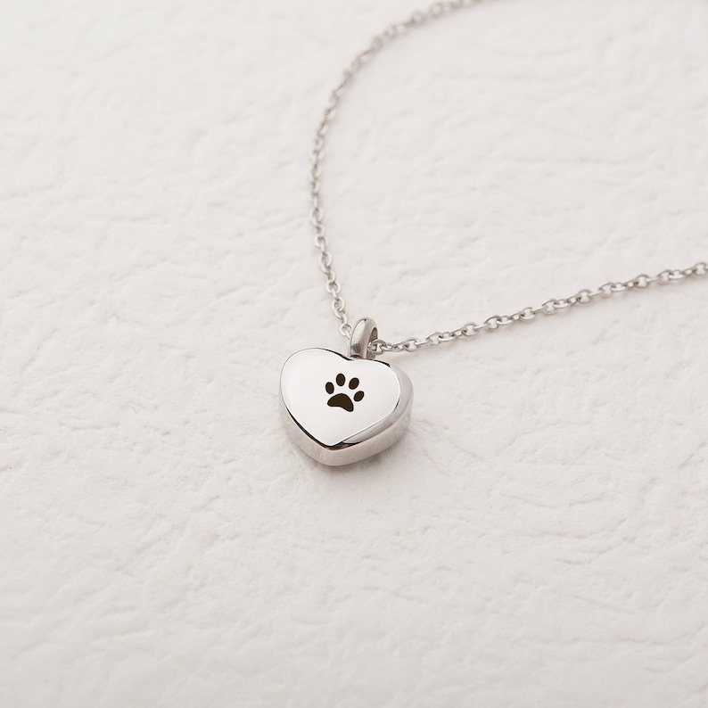May include: A silver heart-shaped pendant necklace with a paw print cutout. The necklace is on a white background.