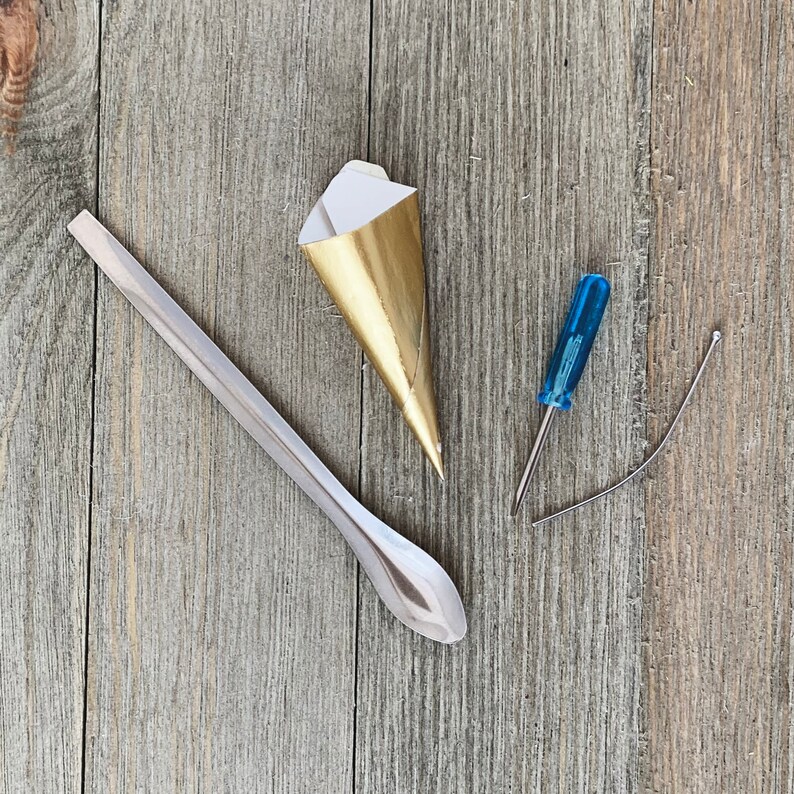 May include: A gold-colored piping bag, a small silver spoon, a blue screwdriver, and a silver wire on a wooden surface.