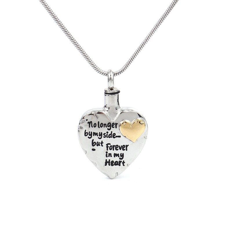 May include: Silver heart-shaped cremation necklace with a gold heart accent. The necklace features the inscription "No longer by my side... but forever in my heart."