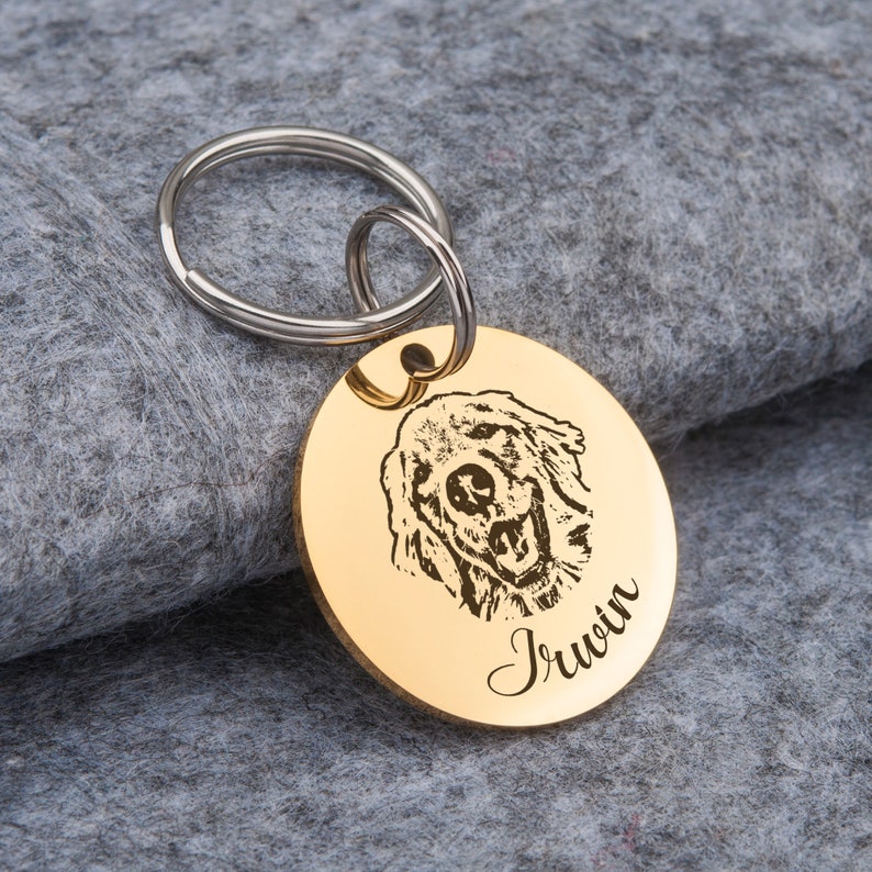 May include: Gold-colored round dog tag with a black and white engraved image of a dog's head and the name "Irwin" engraved below the image.
