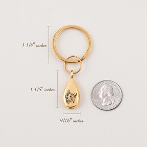 Peut inclure: Porte-cl&eacute;s dor&eacute; avec un charme en forme de larme repr&eacute;sentant un portrait d'animal de compagnie. Le charme mesure 3,2 cm de haut et 1,4 cm de large. Le porte-cl&eacute;s mesure 3,2 cm de diam&egrave;tre.