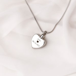 May include: Silver heart-shaped cremation necklace with a small heart and the inscription "John 06.14.2022".