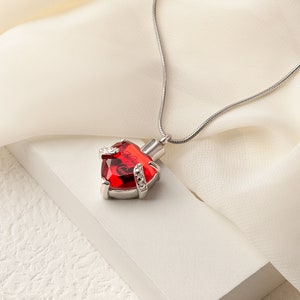May include: A silver chain necklace with a red heart-shaped pendant. The pendant has a silver trim and is engraved with the words "Always in my heart".