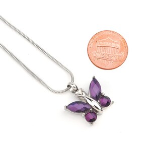 May include: A silver chain necklace with a purple butterfly pendant. The butterfly has clear rhinestones on its wings. The pendant is about the size of a US penny.