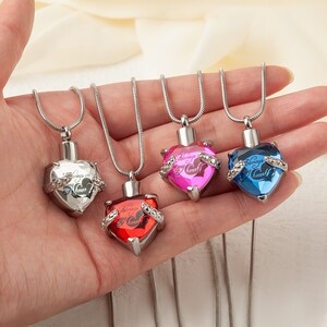 May include: Four silver heart-shaped cremation necklaces with different colored crystals. Each pendant has the inscription "Always in my heart".
